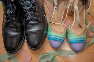 Black lace-up boots beside colorful green and purple strappy heels on a wooden floor.