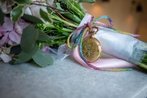 Gold pocket watch with colorful ribbon bow on a bridal bouquet of pink roses and eucalyptus.