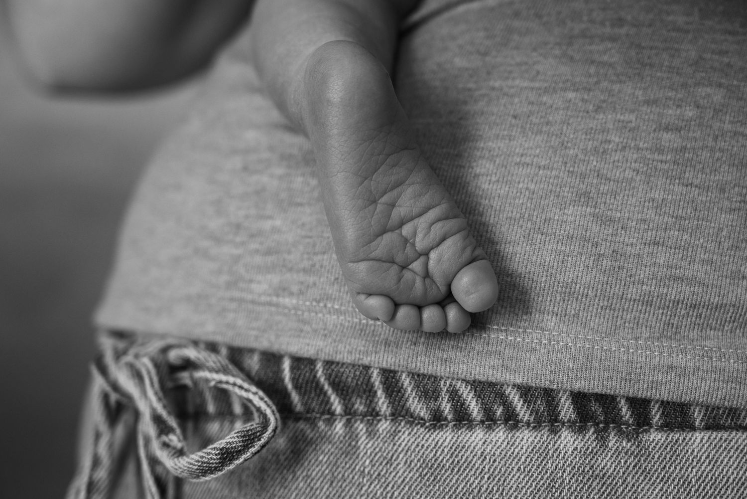 Black and white close-up photo of a newborn baby's tiny foot resting on a parent's lap.