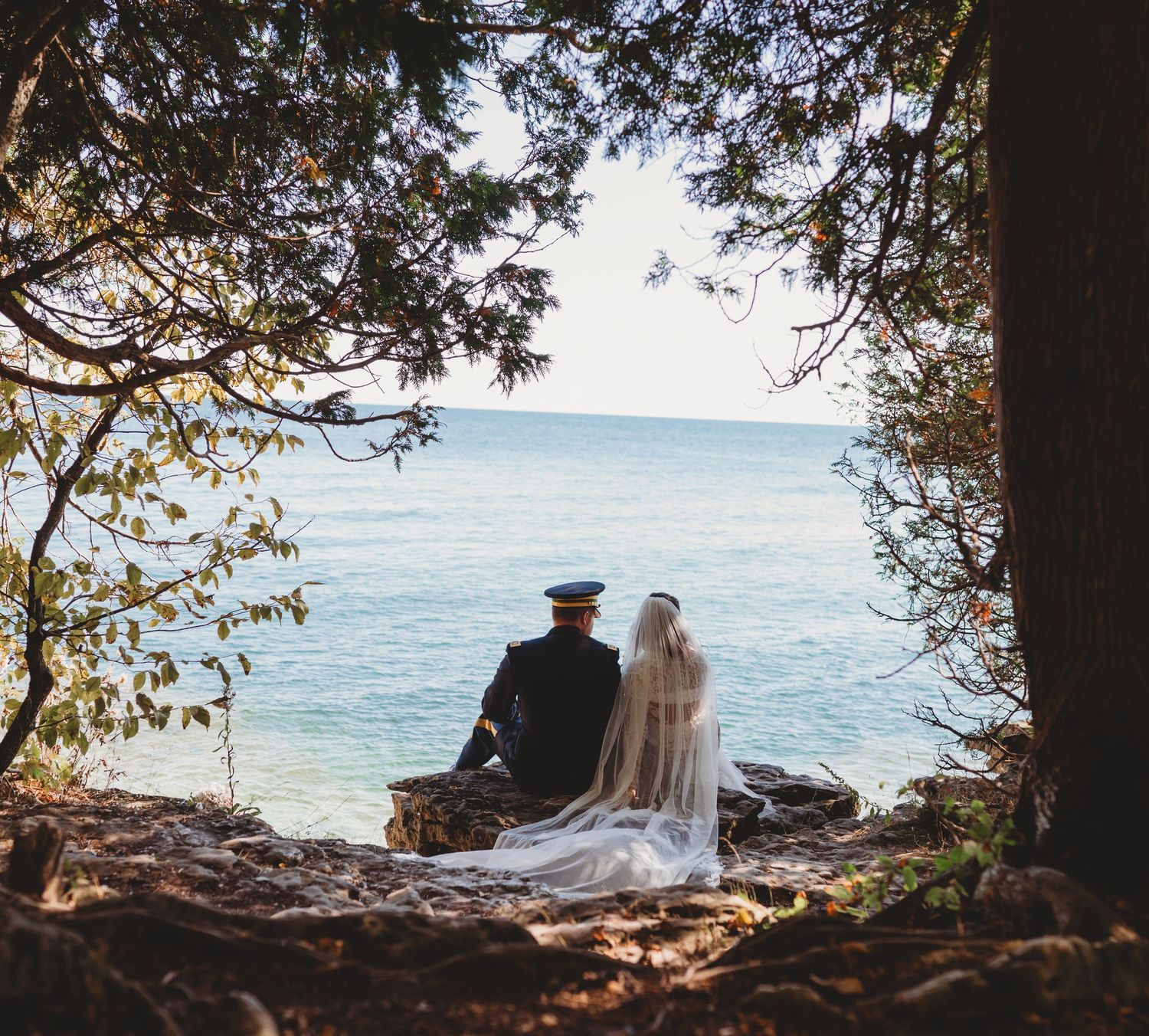 A groom kisses his smiling bride on the cheek as her veil flows in the breeze during an outdoor wedding.