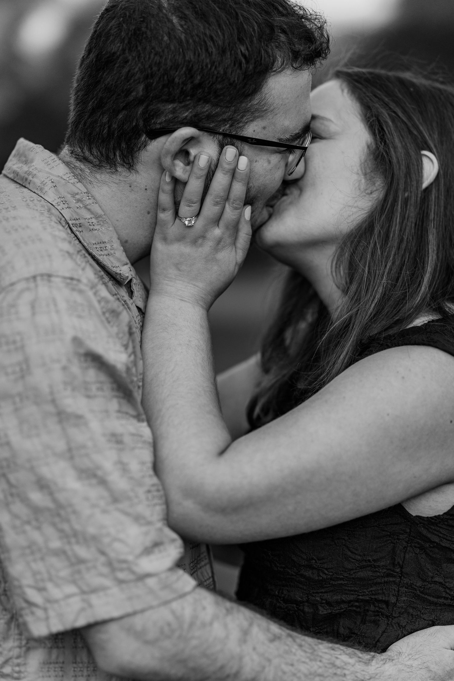 Black and white photo of a couple sharing a romantic kiss, woman wearing an engagement ring.