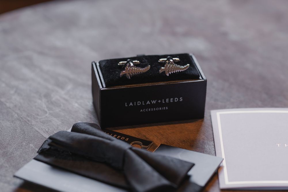 Laidlaw and Leeds silver cufflinks displayed in a black branded box with a gray cloth pouch on a wooden surface.
