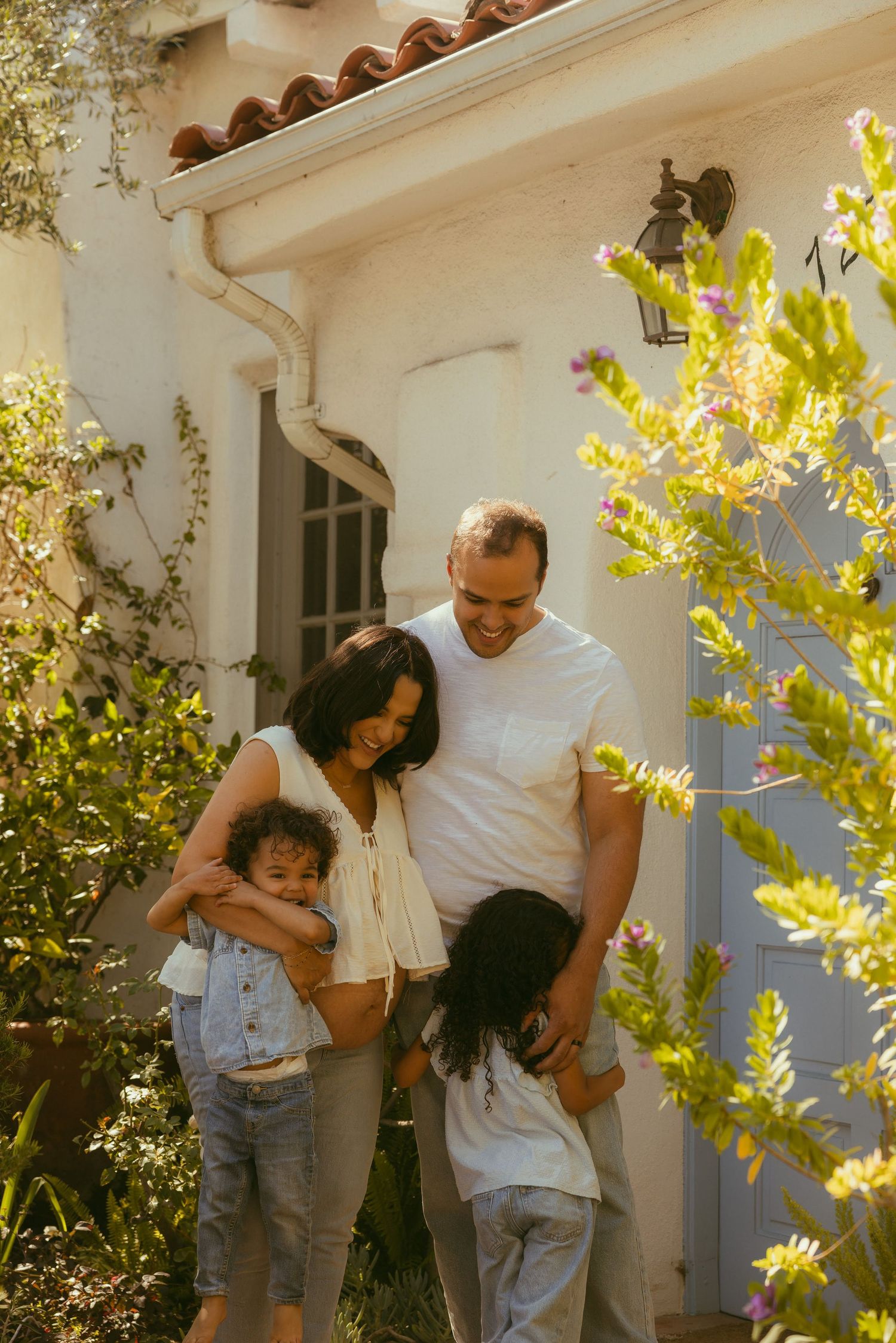 Happy family of four smiling together outside their  home during their unposed family photo session.