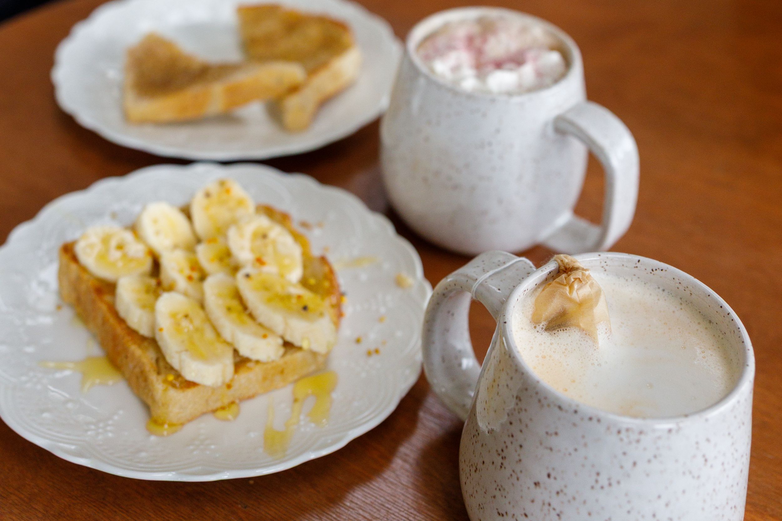 French toast topped with banana slices and honey on a white plate, served with two mugs of hot cocoa topped with marshmallows.