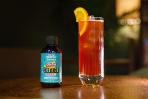 Batched Cocktails Sassy Coffee liqueur bottle beside a tall amber cocktail garnished with an orange slice.
