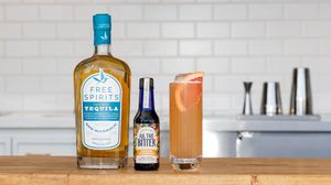 Free Spirits Tequila bottle with a bitters bottle and pink cocktail on a white marble kitchen counter.