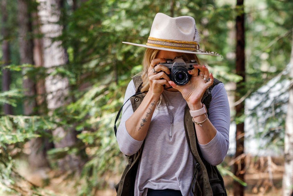 Woman in straw hat photographing in forest with vintage camera and backpack.