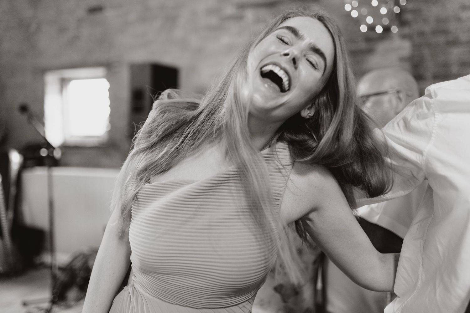 Black and white photo of a joyful woman laughing and dancing with long flowing hair at an indoor event.