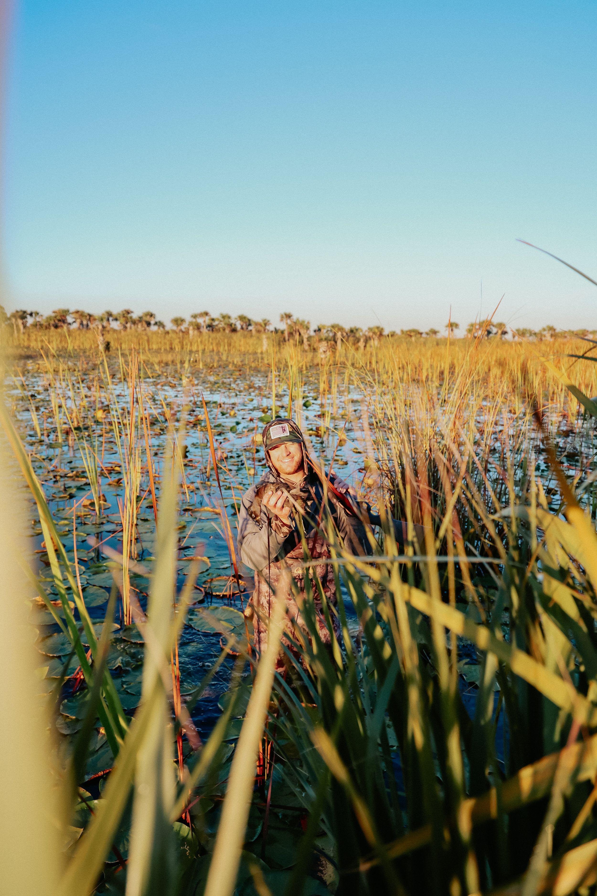 Female hunter in camouflage waders standing in marsh wetland during duck hunting.