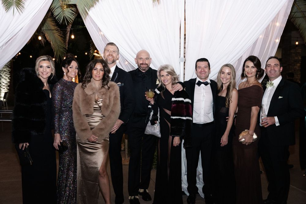 Group of elegantly dressed guests posing together at a formal gala event with white draping decor.