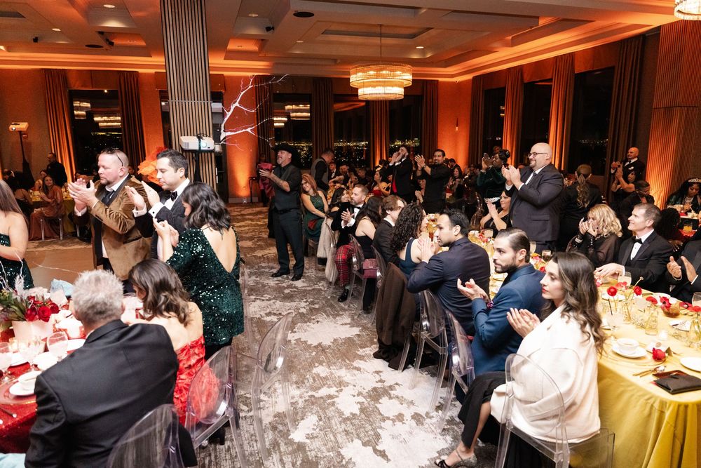 Elegant gala event with guests in formal attire seated at decorated tables in a warmly lit ballroom.
