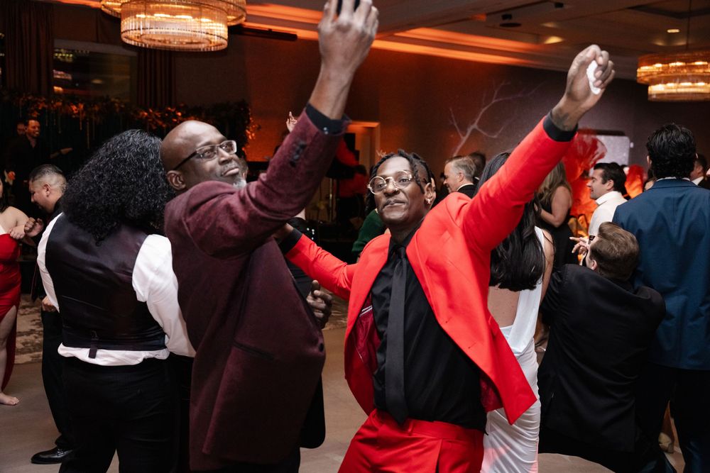 People dancing joyfully at a formal event, man in red suit raises hand on dance floor.
