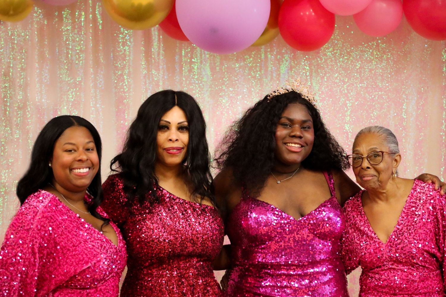 Group wearing matching pink sequin dresses poses with balloons at celebration.