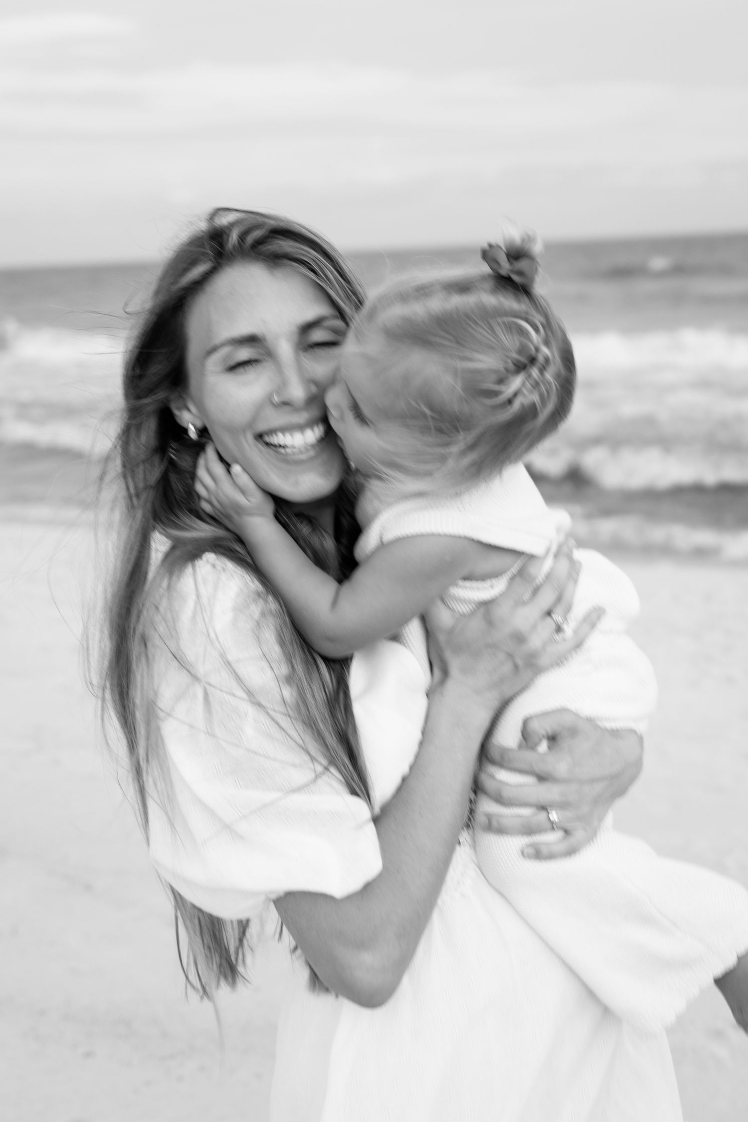 Mother kissing her toddler daughter on the beach in Gulf Shores, Alabama.