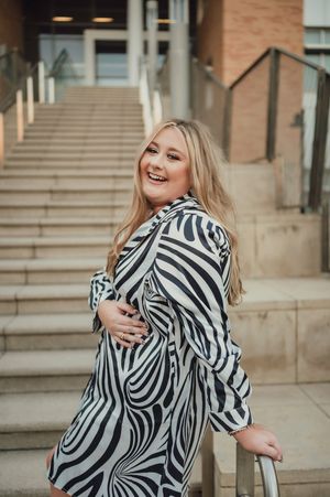 Laughing blonde woman in black and white zebra print dress posing on outdoor stairs.