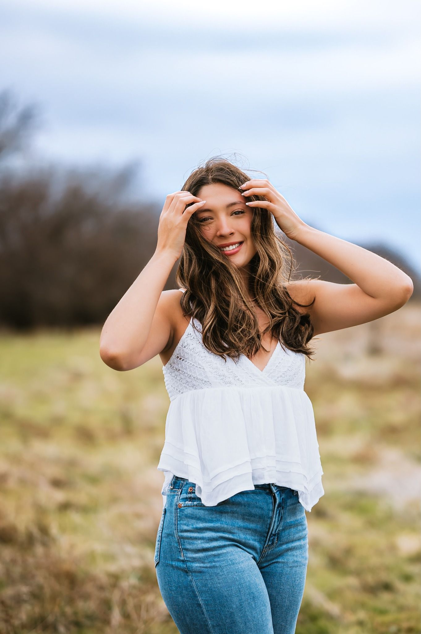 Smiling teenage girl in white top and jeans posing outdoors in a grassy field portrait.