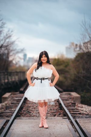 Young woman in white tulle dress and pink cowboy boots posing on railroad tracks in the city.