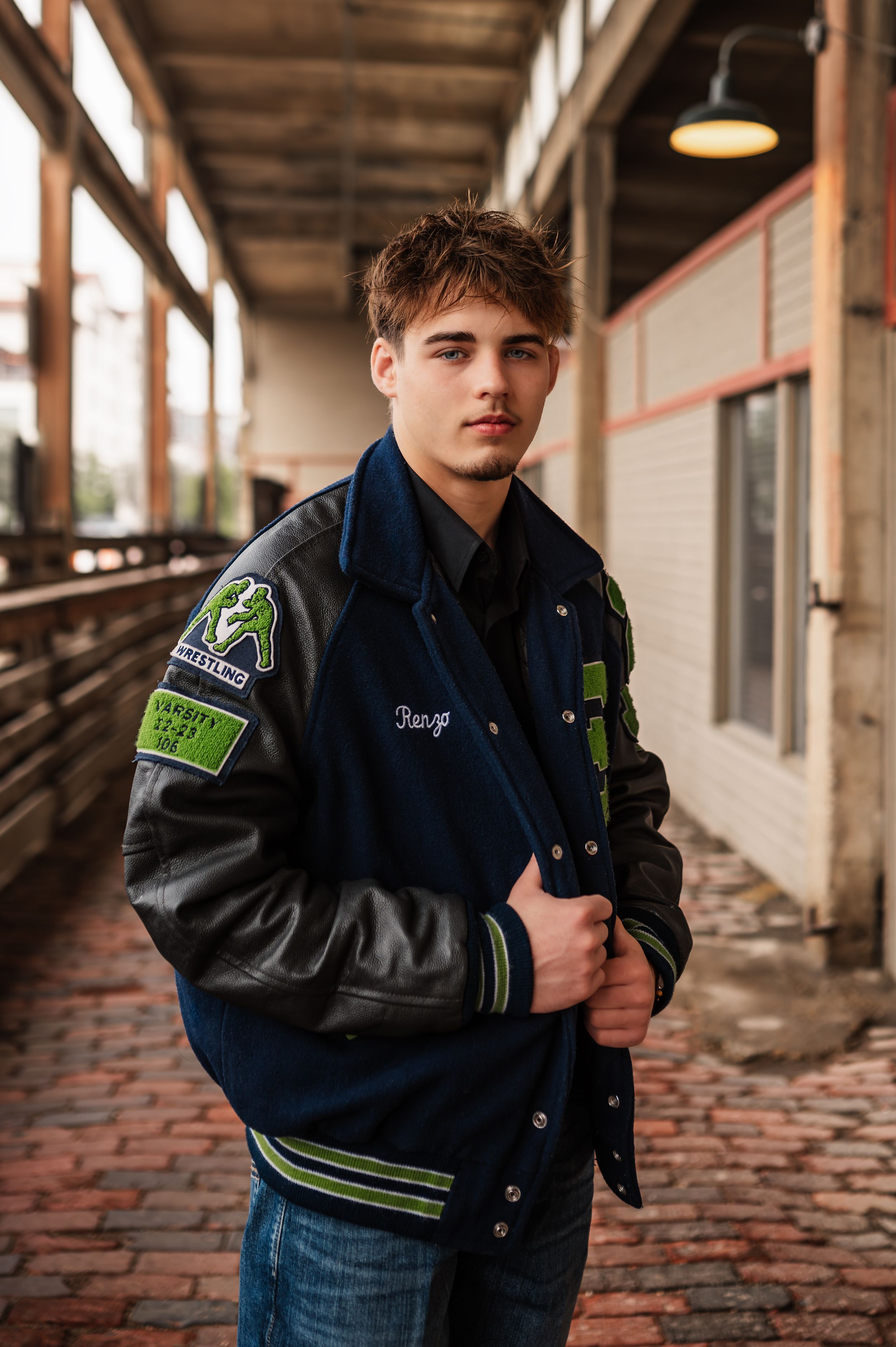Young man in a blue and black varsity letterman jacket posing in an urban hallway setting.