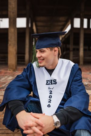 Smiling male graduate in blue cap and gown with EHS Class of 2026 stole seated outdoors.