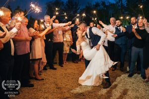 Wedding celebration with sparklers creating light trails as guests surround dancing couple.