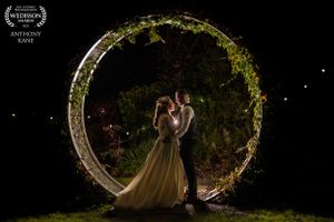 Couple posing under illuminated floral arch at night with twinkling lights in this award winning photo