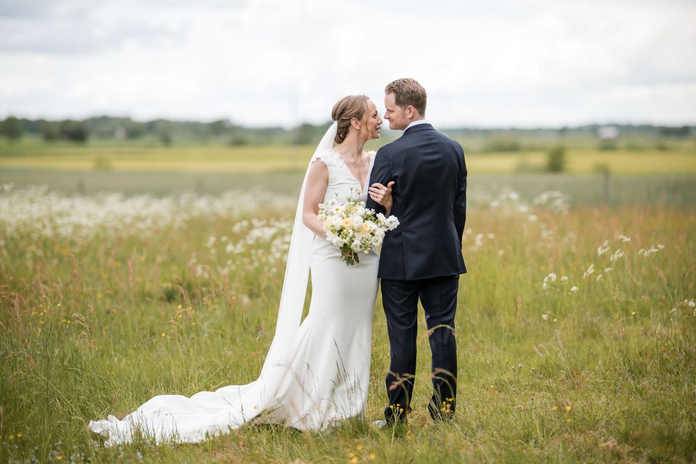 Bride and groom share a romantic kiss in a wildflower meadow, bride in elegant white gown holding bouquet.