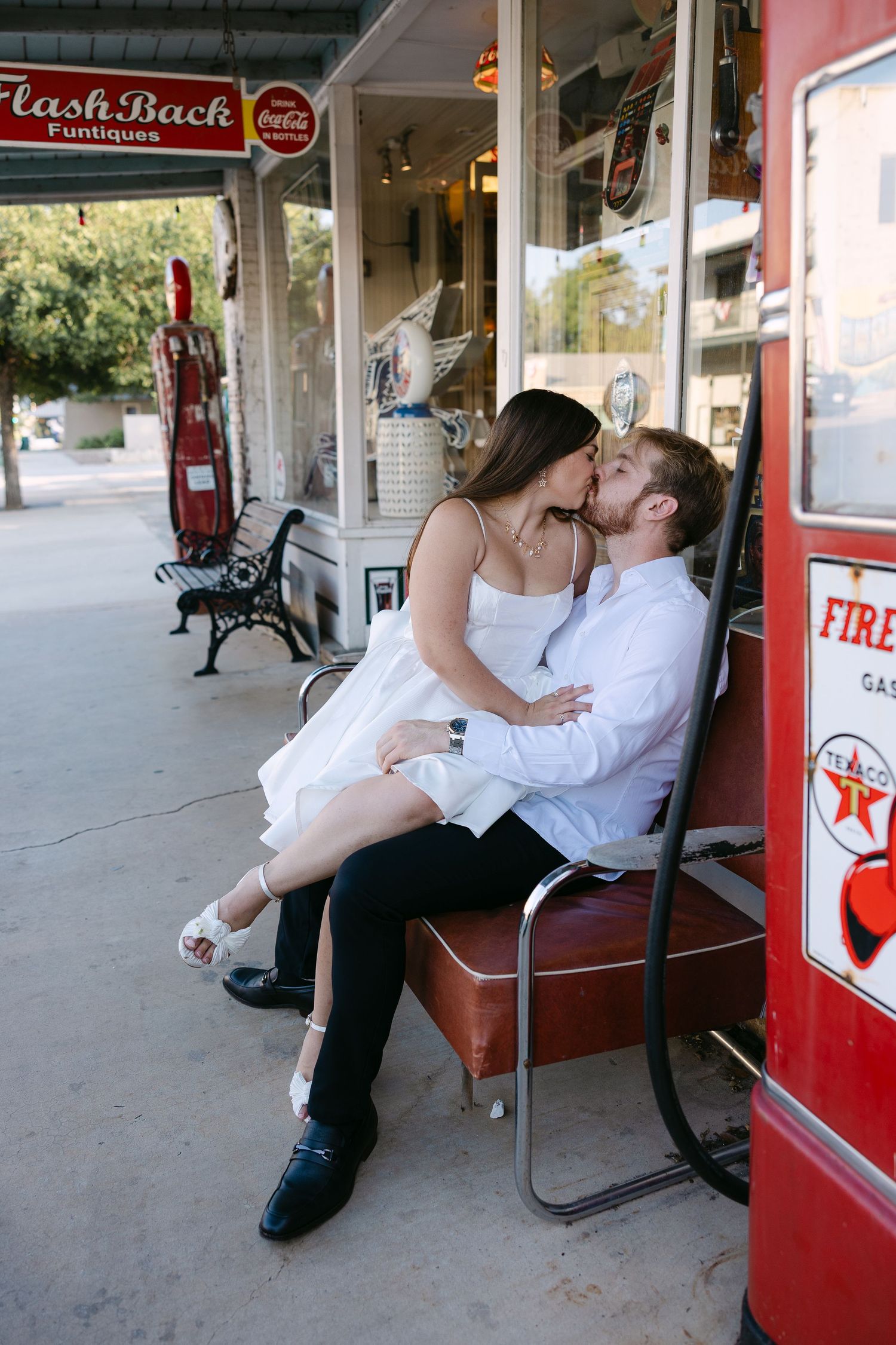 Couple sharing a romantic kiss outside a vintage Flash Back Funtiques antique shop with retro Texaco gas pumps.