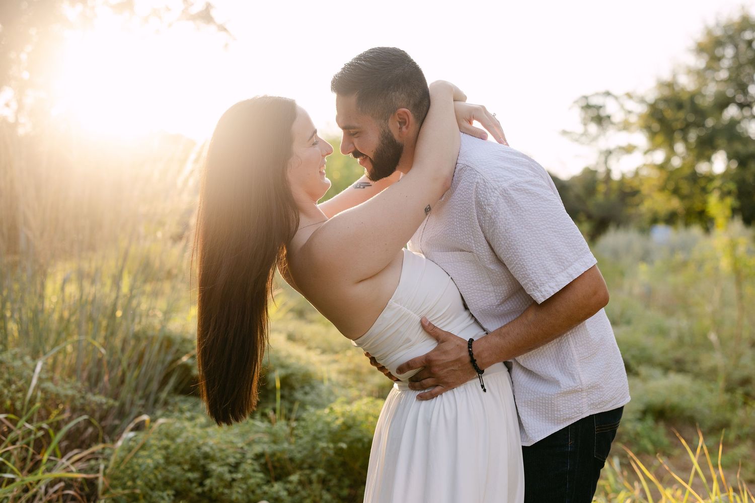 Couple embracing and almost kissing in golden sunset light surrounded by lush green nature outdoors.