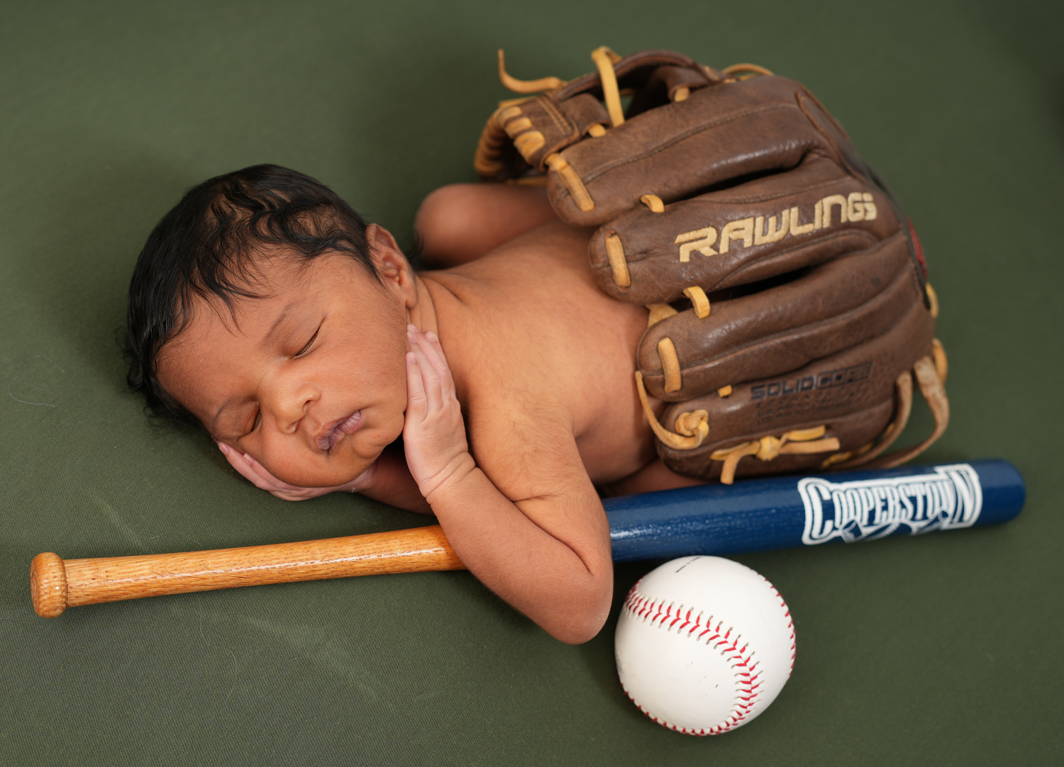 Sleeping newborn photographed with his father’s baseball glove, bat and baseball as part of a personalized newborn session.