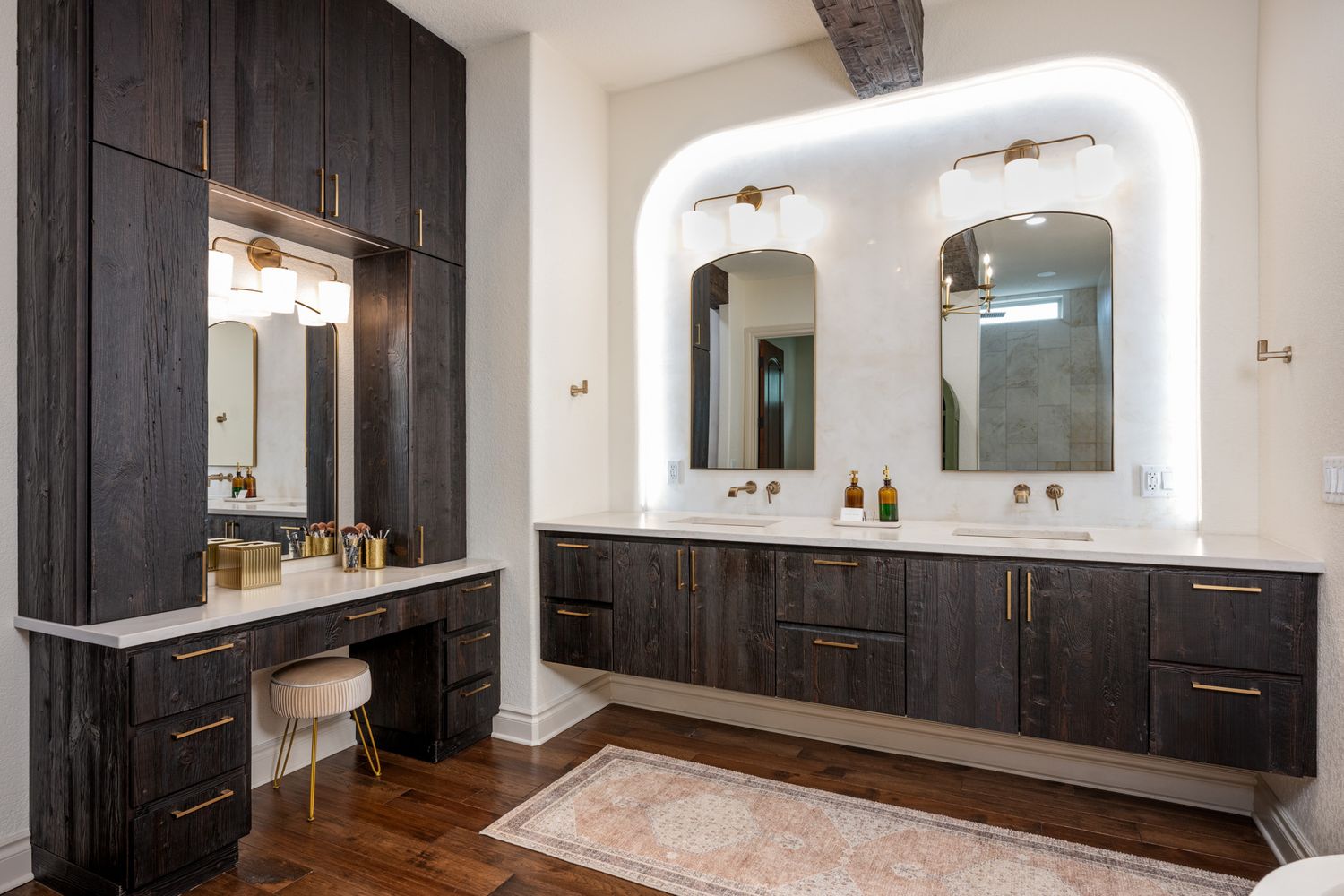 Elegant master bathroom with dark wood cabinets, dual sinks, and arched backlit mirrors.