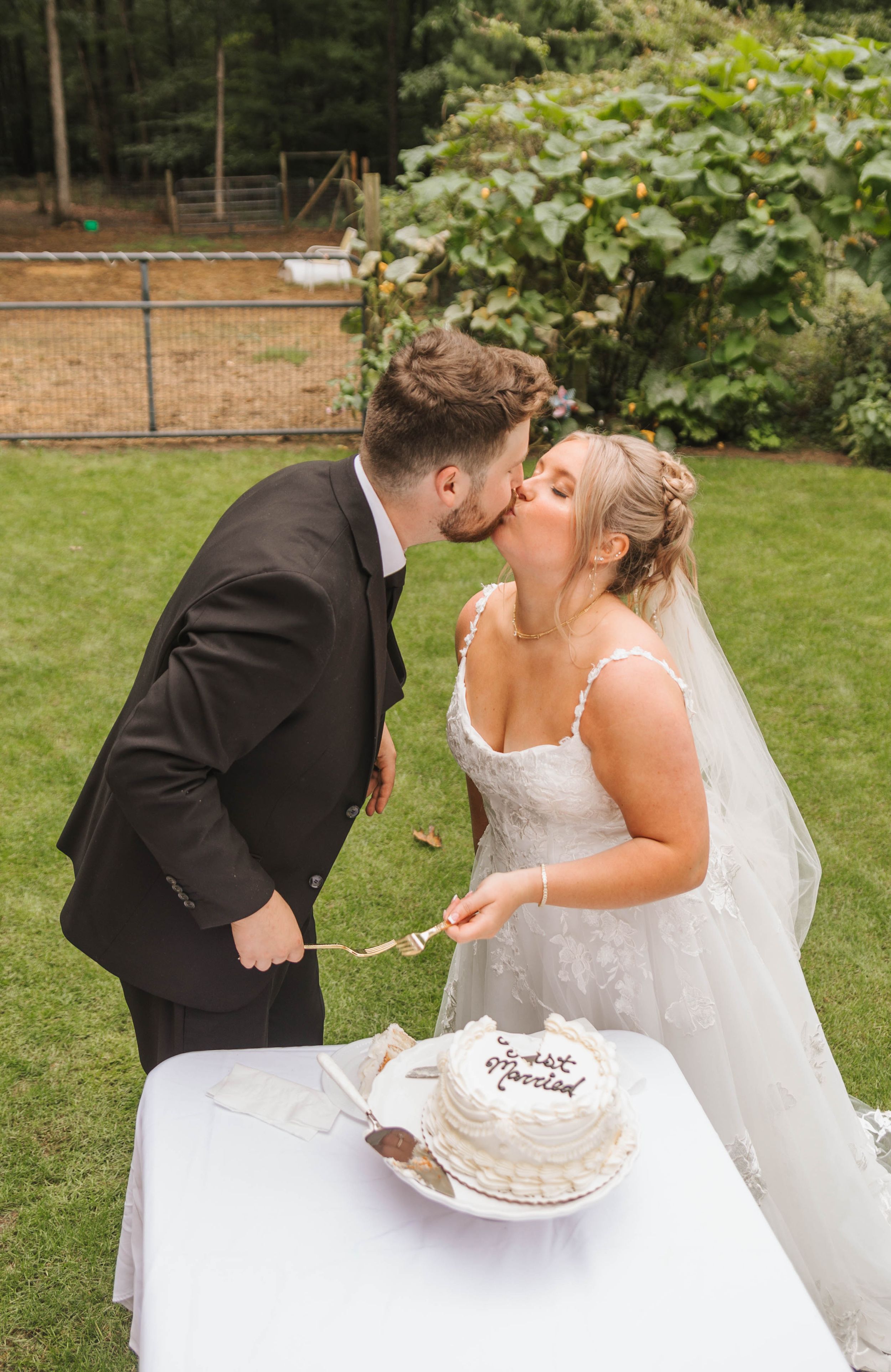 Bride and groom sharing a kiss while cutting their wedding cake outdoors.