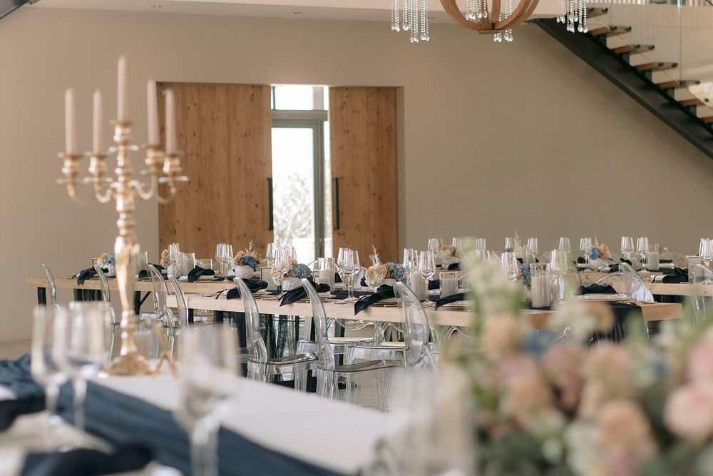 Elegant wedding reception hall with long tables, navy blue napkins, crystal glassware, gold candelabras, and floral centerpieces.