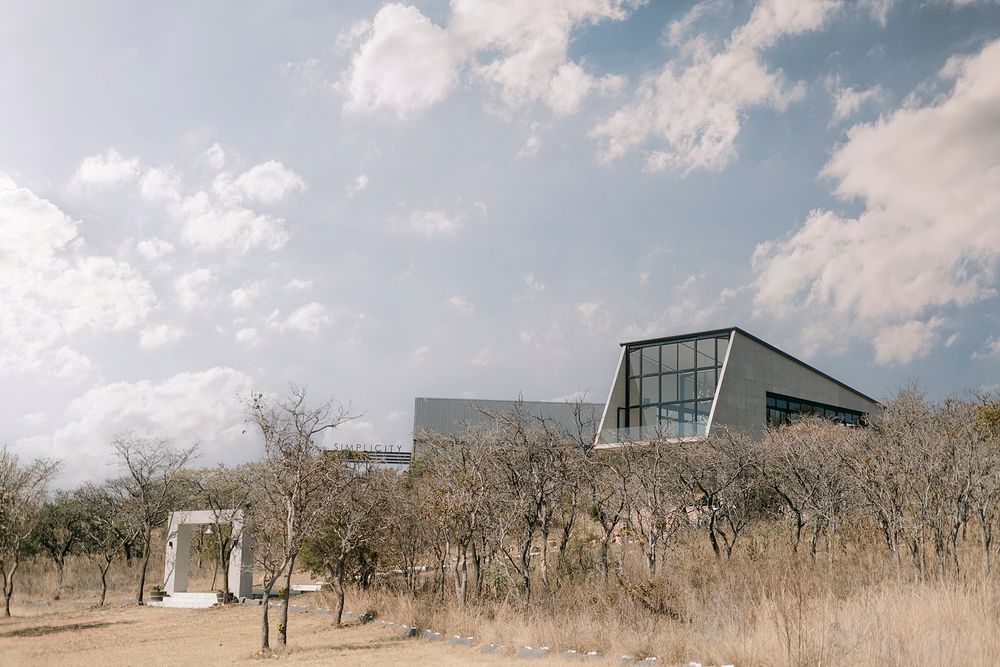 Modern angular building surrounded by bare trees under a partly cloudy sky in an arid landscape.