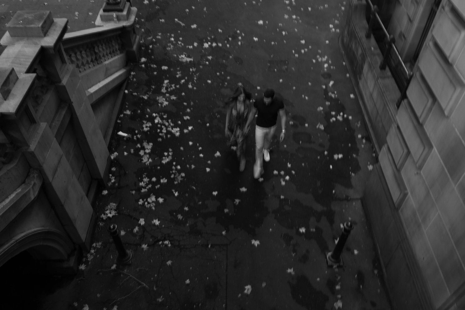 Black and white aerial view of two people walking on a cobblestone street scattered with flower petals.