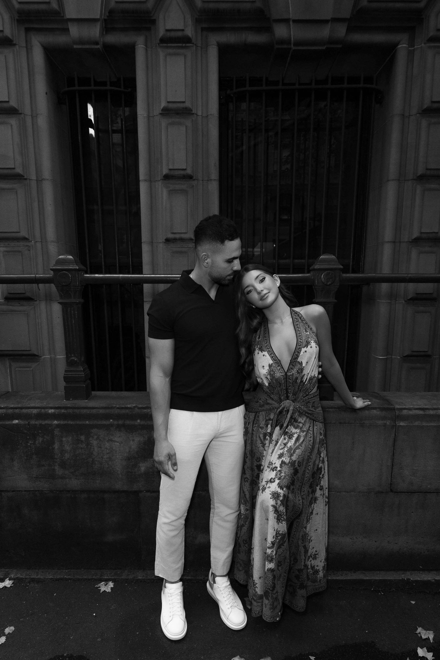 Black and white photo of a stylish couple posing together in front of an ornate building entrance.