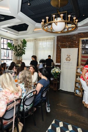 Women gathered at tables in an elegant restaurant with brass chandelier, brick wall, and baby shower decorations.