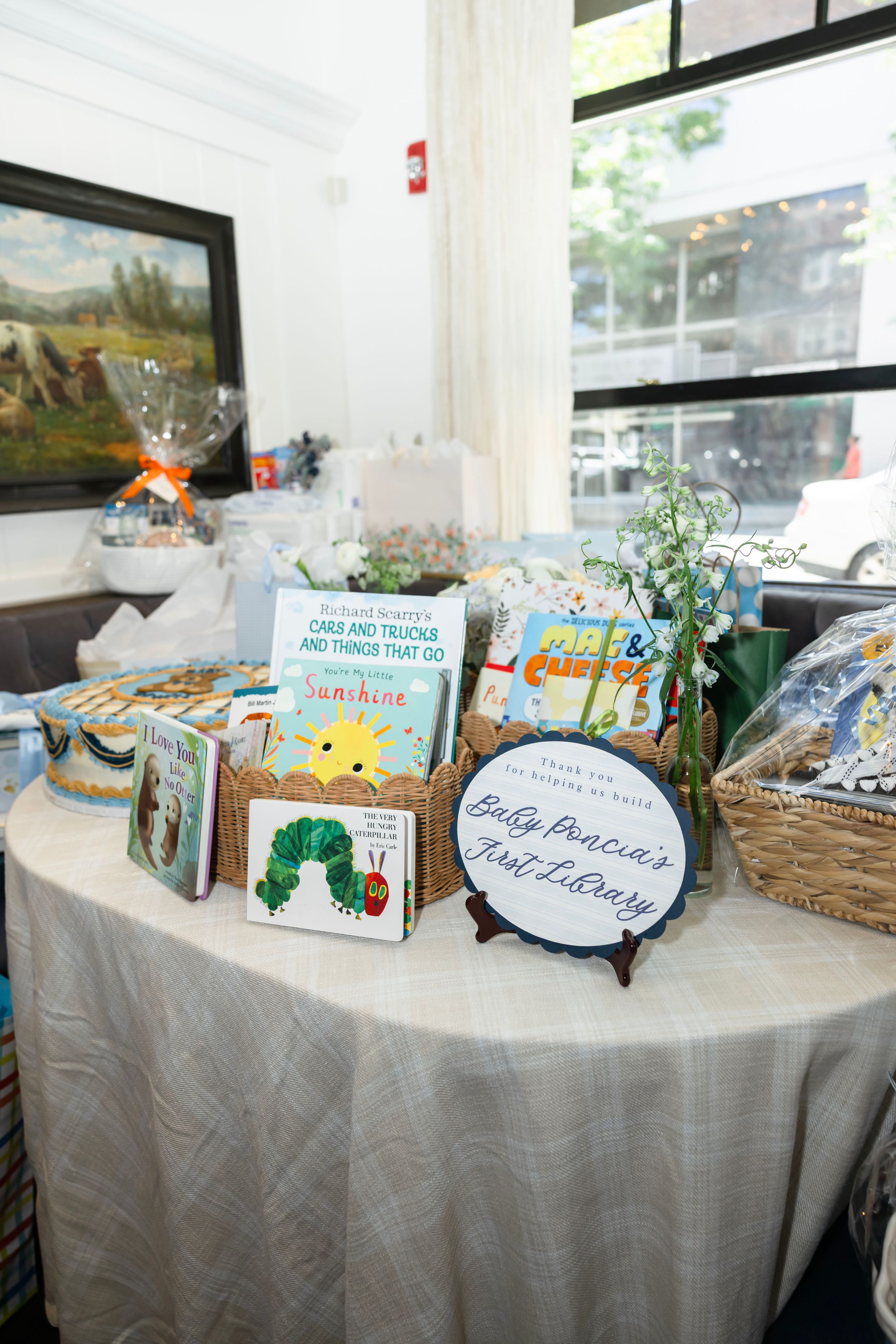 Baby shower book display table with children's books including The Very Hungry Caterpillar and a 'Baby's First Library' sign.