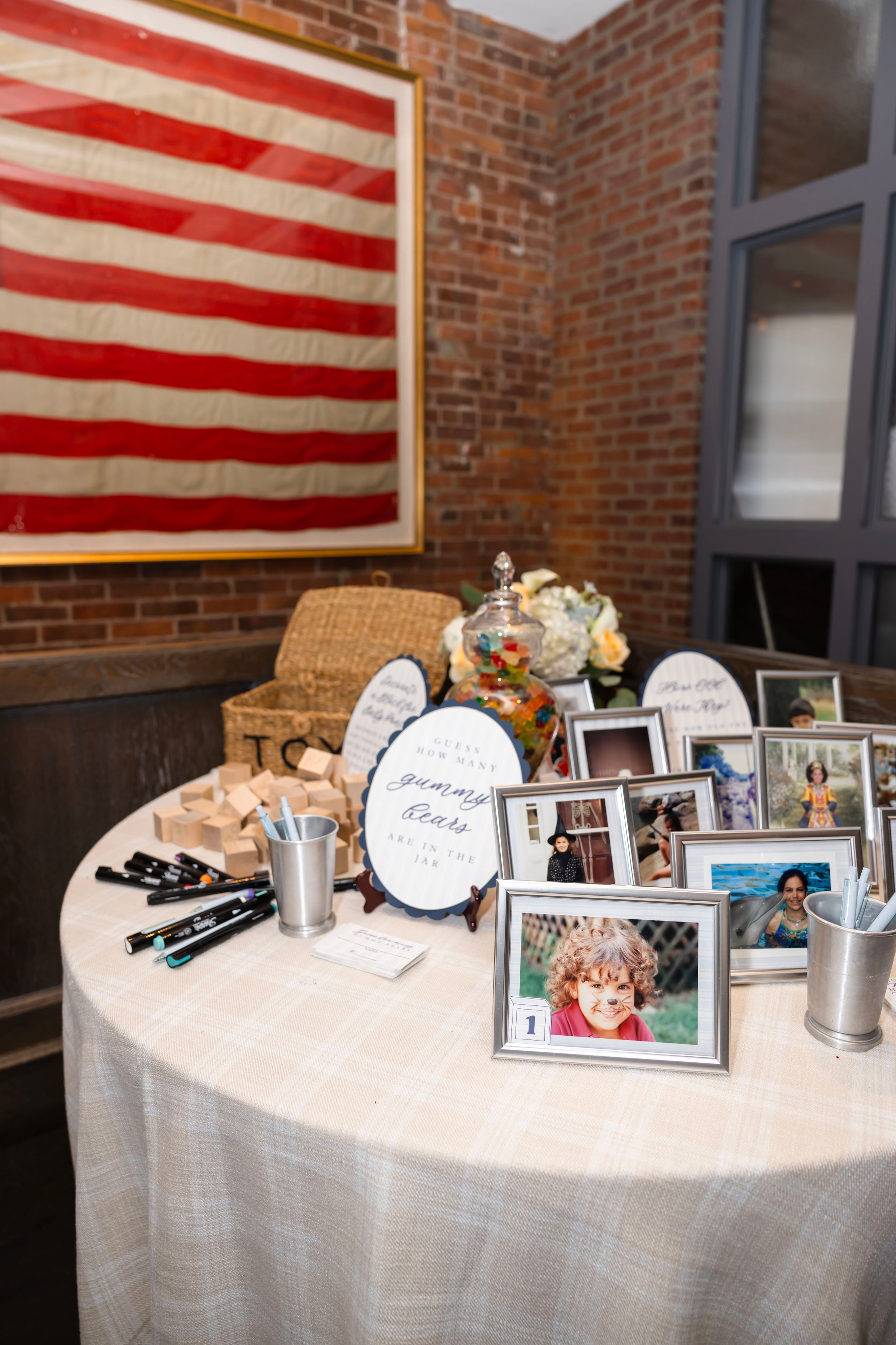 A memorial table with framed photos, markers, and decorative signs displayed beneath an American flag at an event.