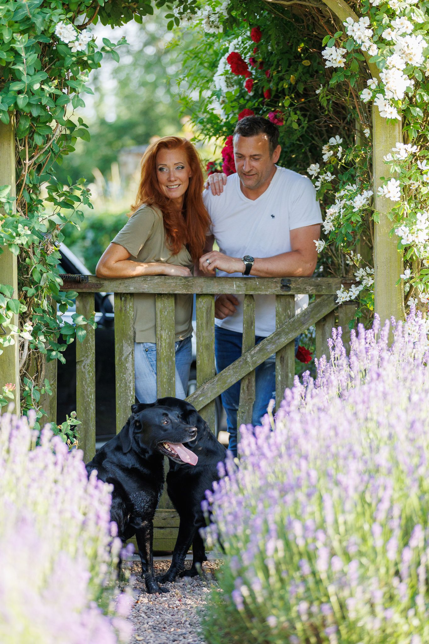 A smiling couple stands with a black and white horse and small dog in front of a white van on a farm.