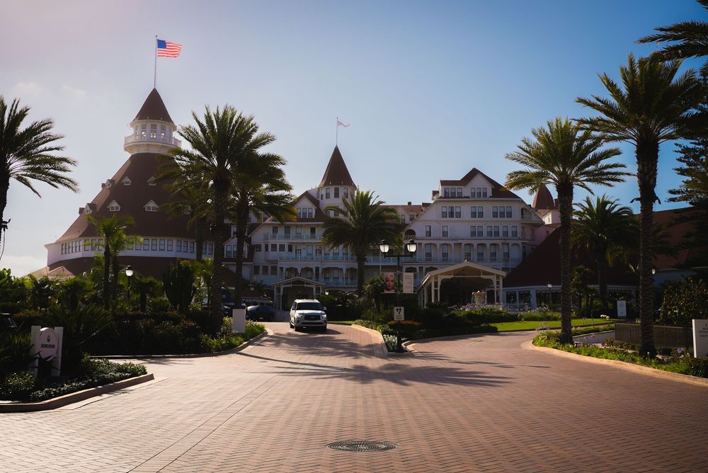 Grand white Victorian hotel entrance with palm trees and American flag on sunny day.