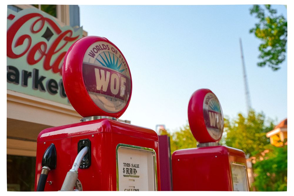 Vintage red World gas pumps with globe tops displayed outside a Coca-Cola market on a sunny day.