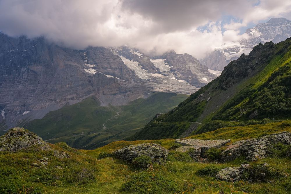 Lush green alpine valley surrounded by dramatic rocky mountains with snow-capped peaks and clouds in the Swiss Alps.