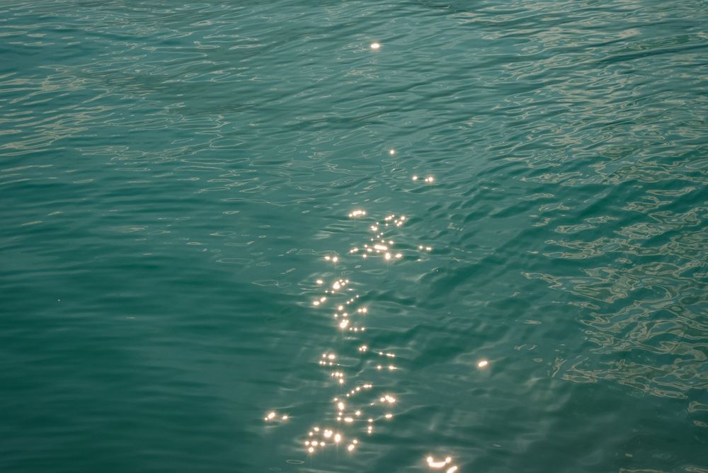 Sunlight sparkles on calm turquoise ocean water surface creating a serene and tranquil seascape.