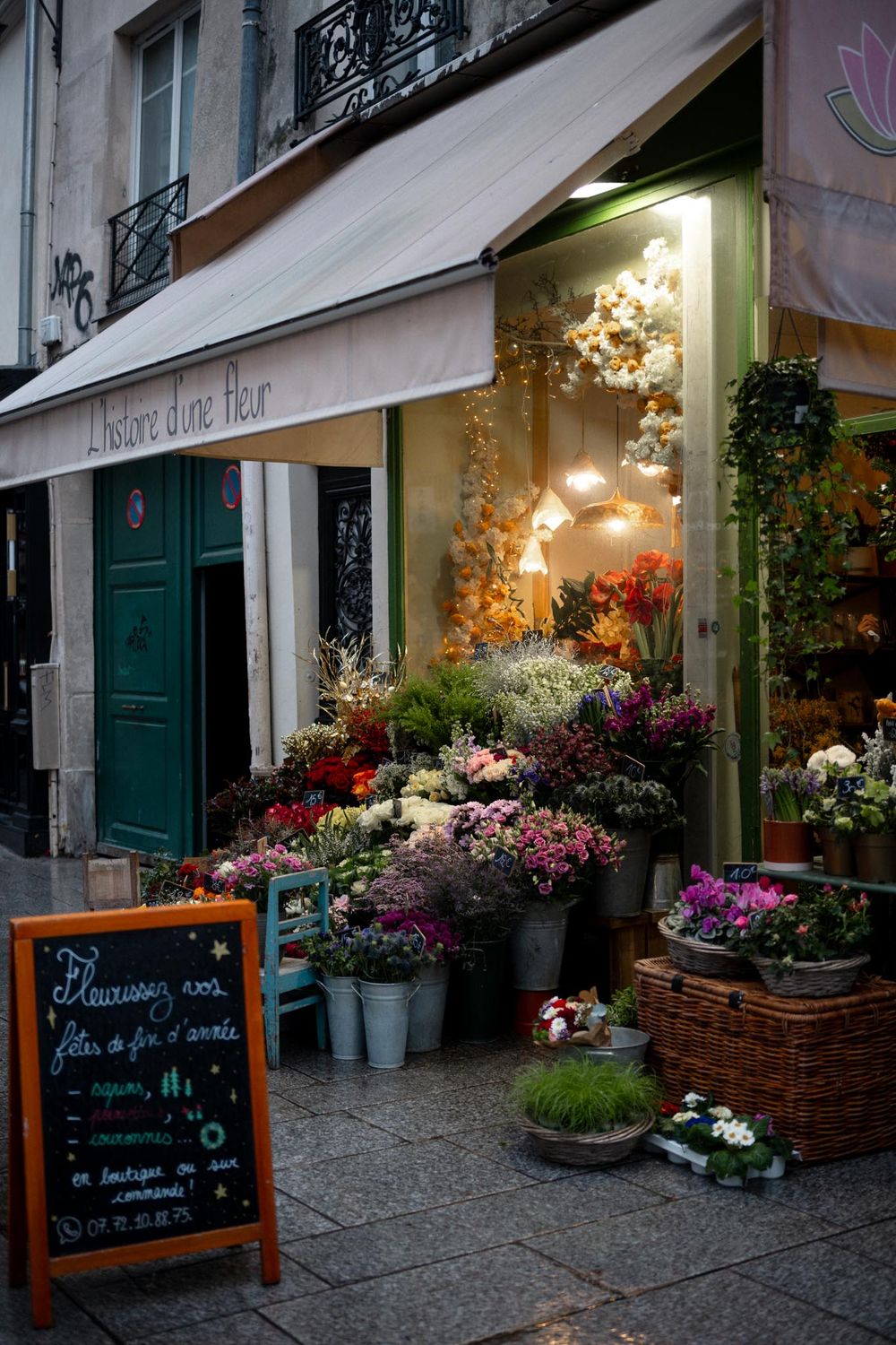 Charming Parisian flower shop L'Histoire d'une Fleur with colorful blooms displayed outside on a cobblestone street at dusk.