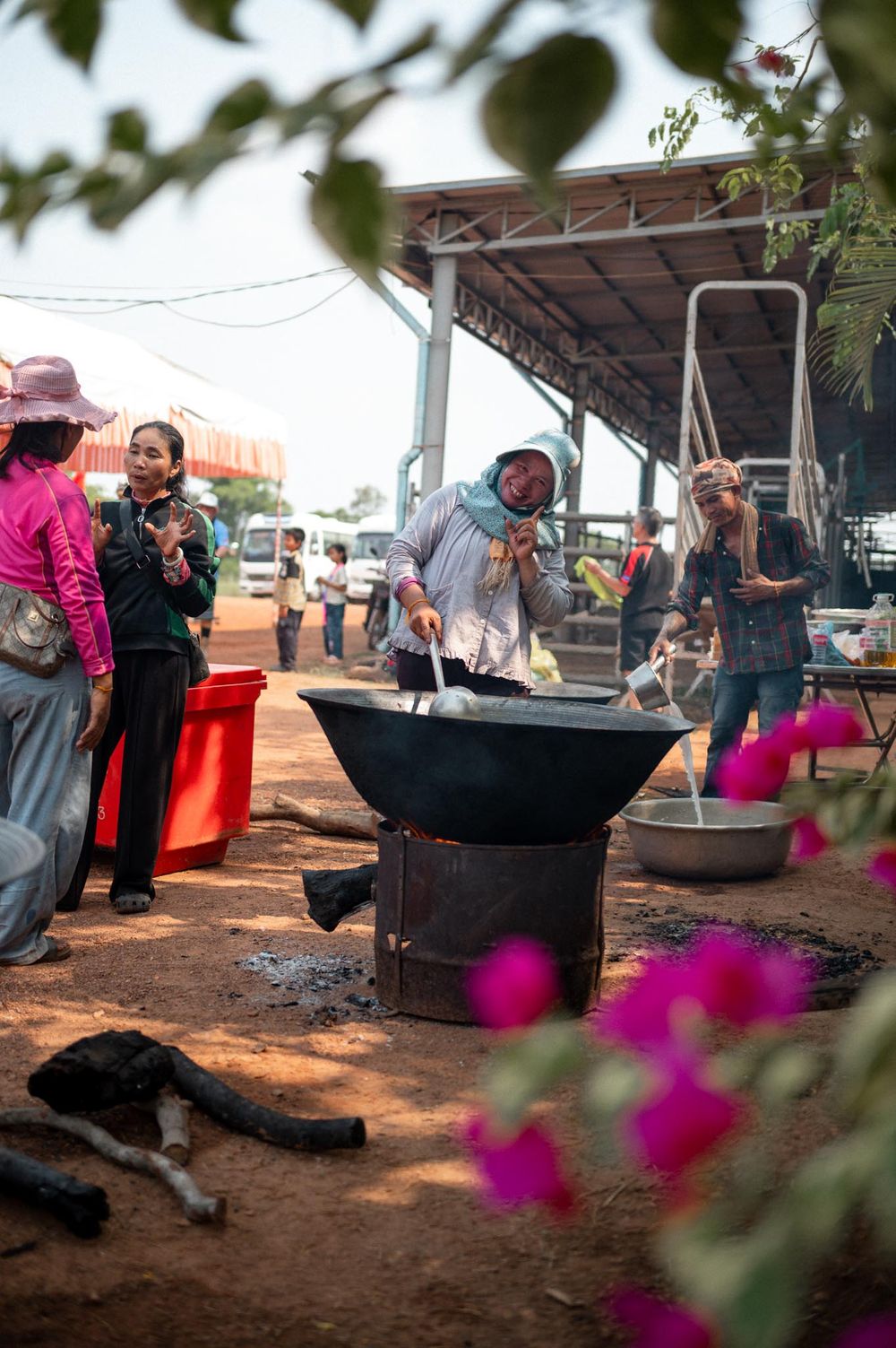 Women cooking over a large wok on an open fire at an outdoor market in Southeast Asia.