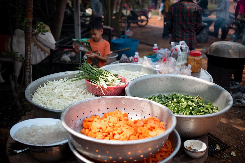 Outdoor market food stall with bowls of fresh chopped vegetables including carrots, green onions, and cabbage.
