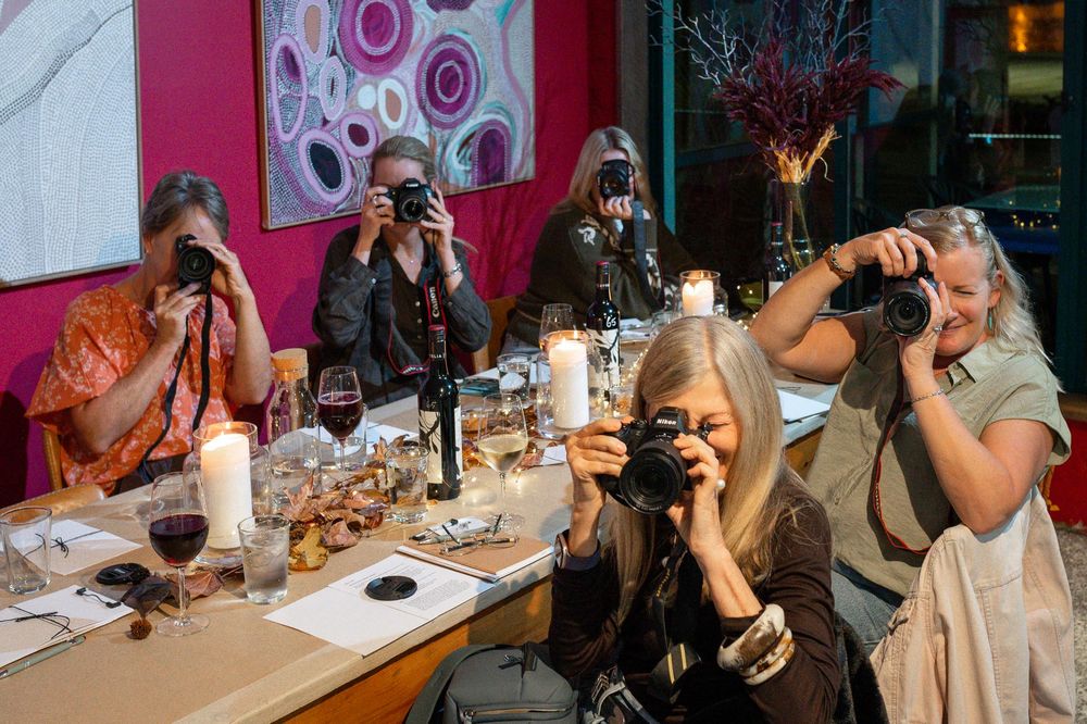 Women photographers capturing images at a stylish dinner table with candles, wine glasses, and pink decor in background.