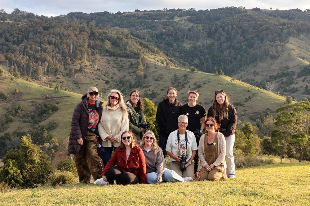 Group of women posing on green hillside with scenic mountain landscape in background on a sunny day.