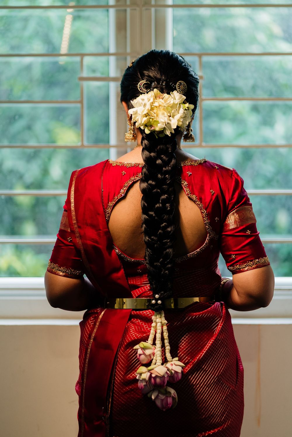 Indian bride in red saree showing elaborate braided hair adorned with white flowers and pearl accessories.