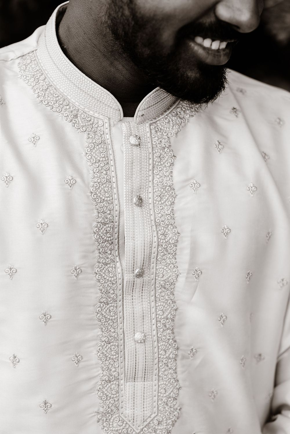 Black and white photo of a smiling man wearing an embroidered white kurta with decorative buttons.